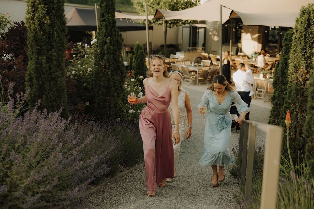 Wedding guests mingle and walk through an outdoor garden venue with lush greenery and natural lighting.