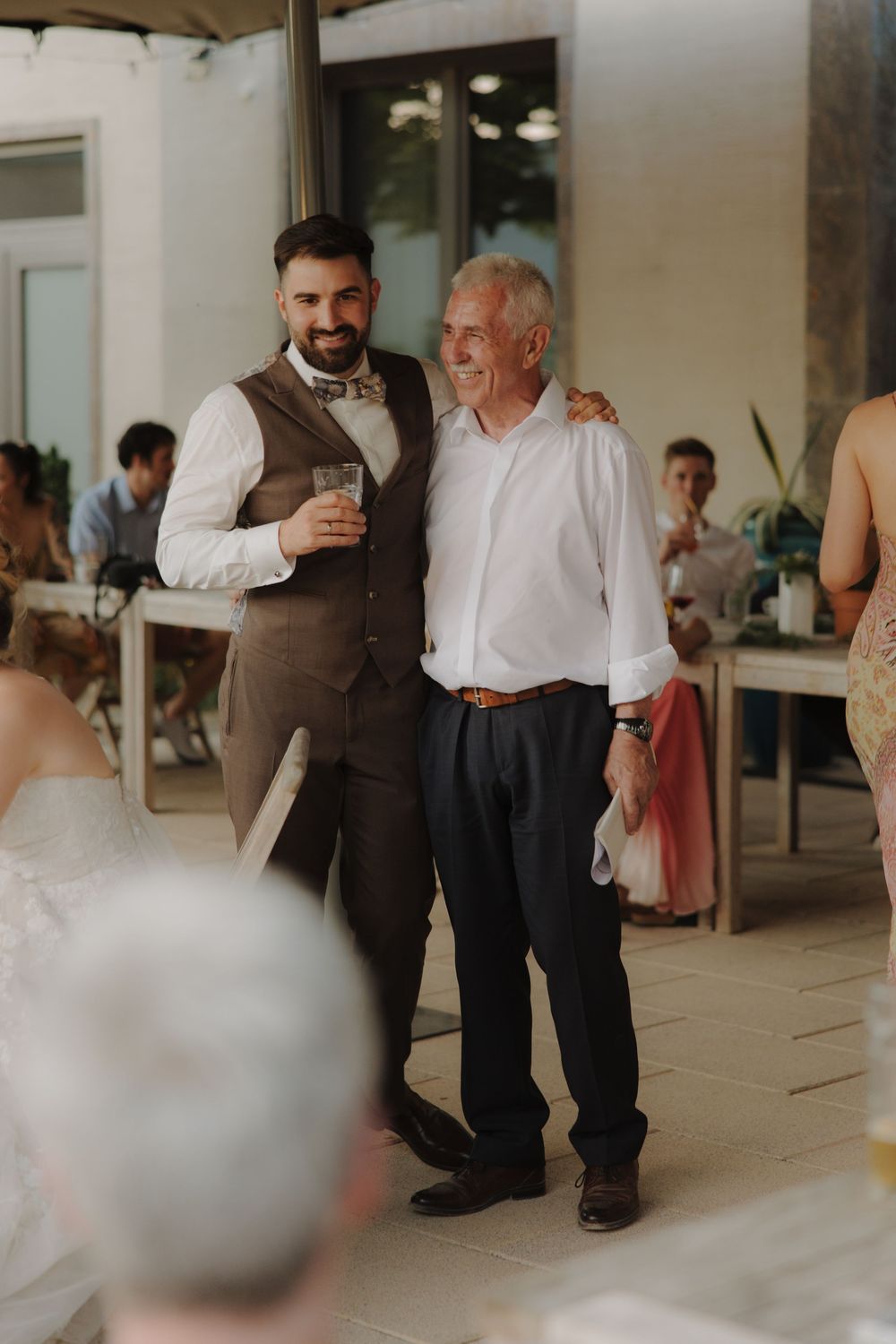 Wedding reception guests gather in a bright indoor venue with casual conversation and mingling.