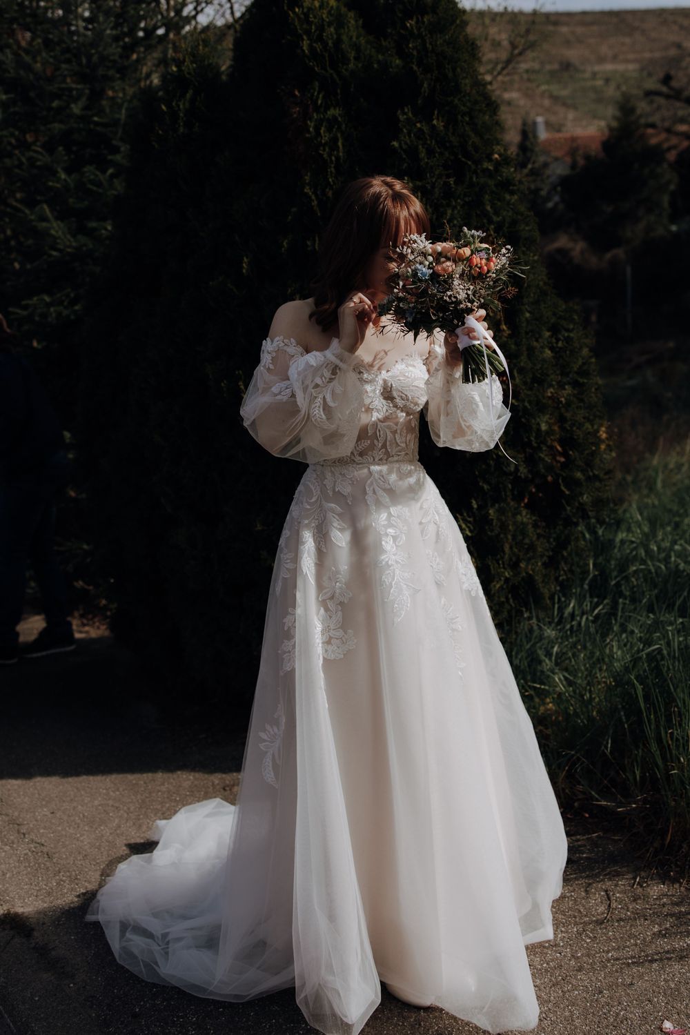 Two matching white floral dresses with puffed sleeves and tulle skirts stand side by side in an outdoor garden setting.