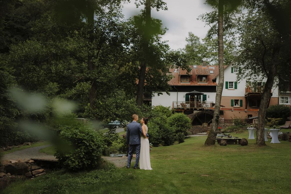 A scenic outdoor wedding ceremony setup with chairs arranged on a lush green lawn surrounded by trees.