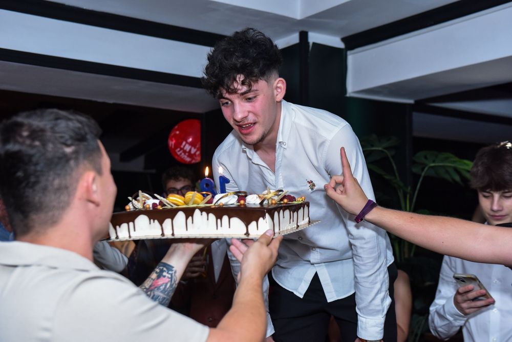 People gather around a long table with desserts and candles in a dimly lit restaurant setting.