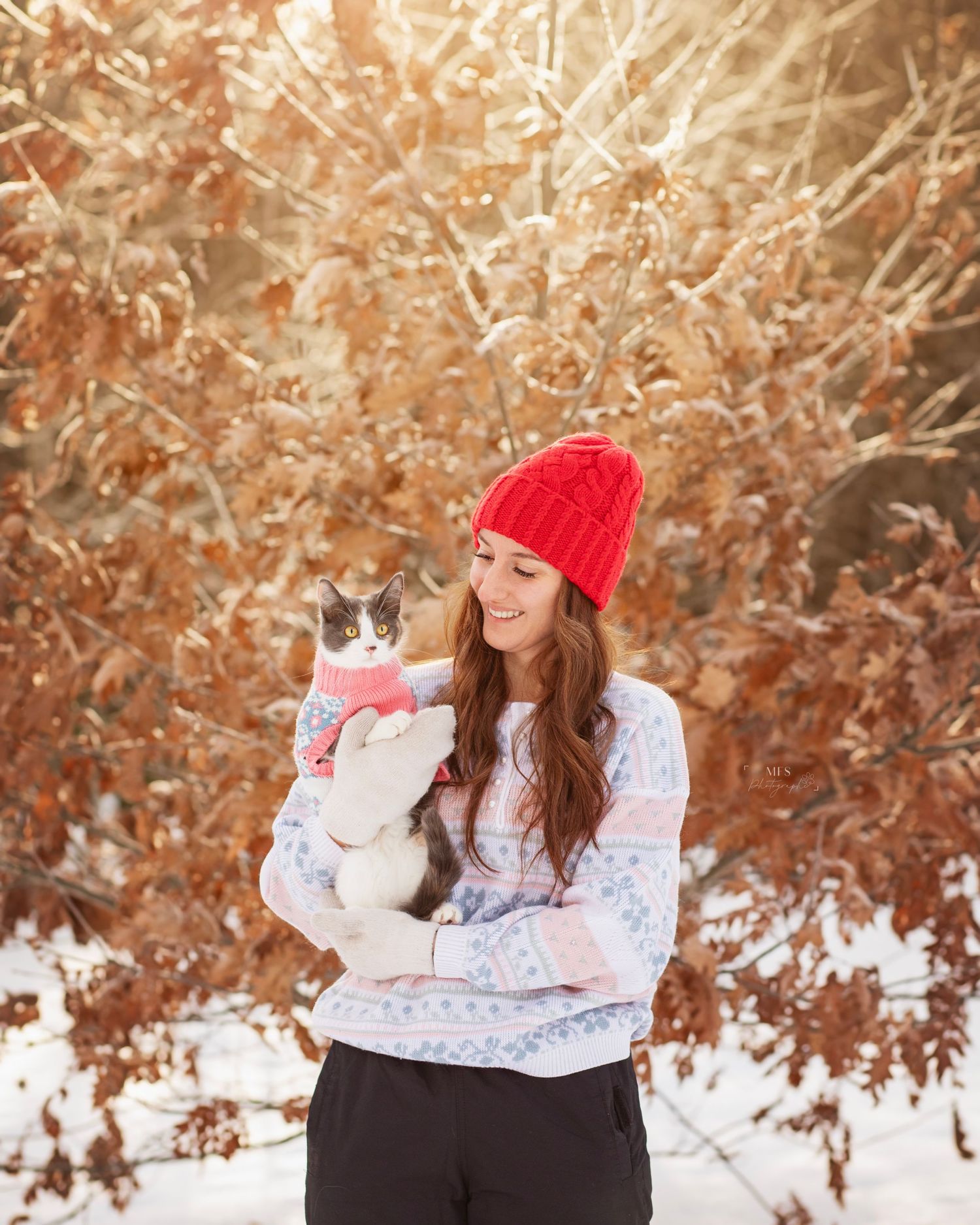 Girl with read beanie holding her cat in a winter scenery