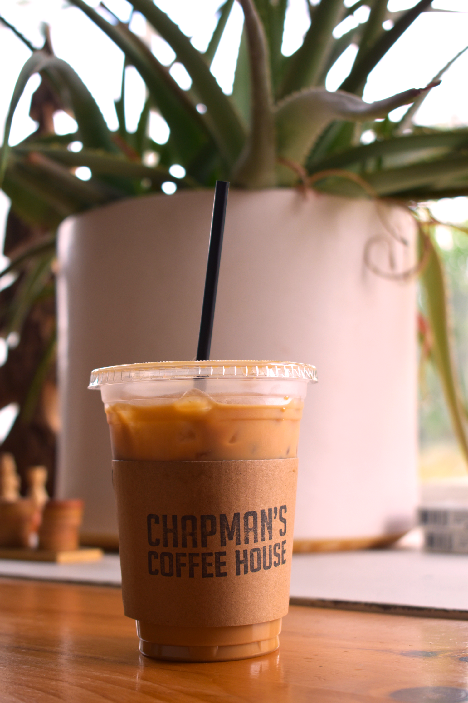 An iced coffee drink from Chapman's Coffee House sits on a wooden table with a plant in the background.