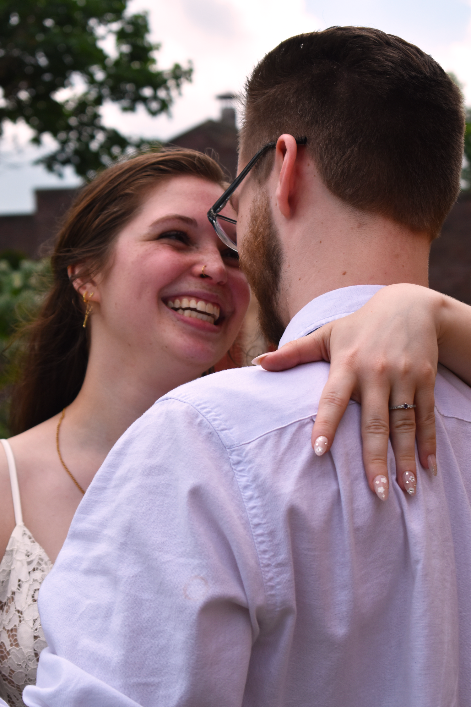 Intimate moment between couple showing engagement ring outdoors.