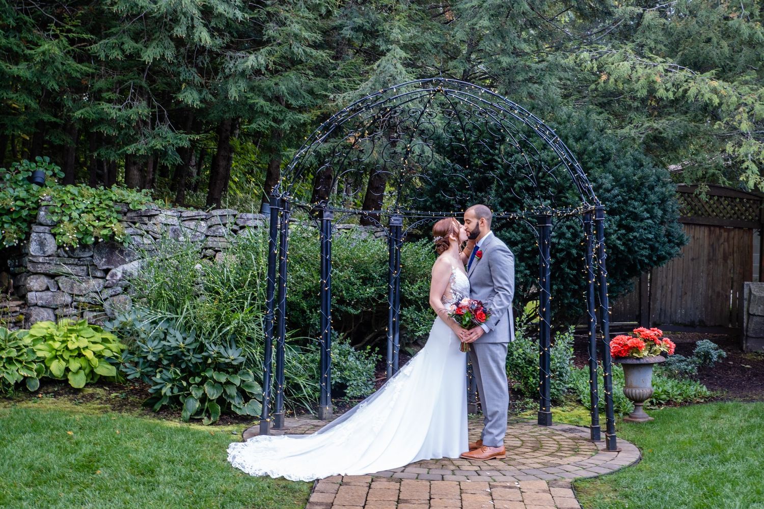 Romantic wedding ceremony under a garden arch with lush greenery and stone wall backdrop.