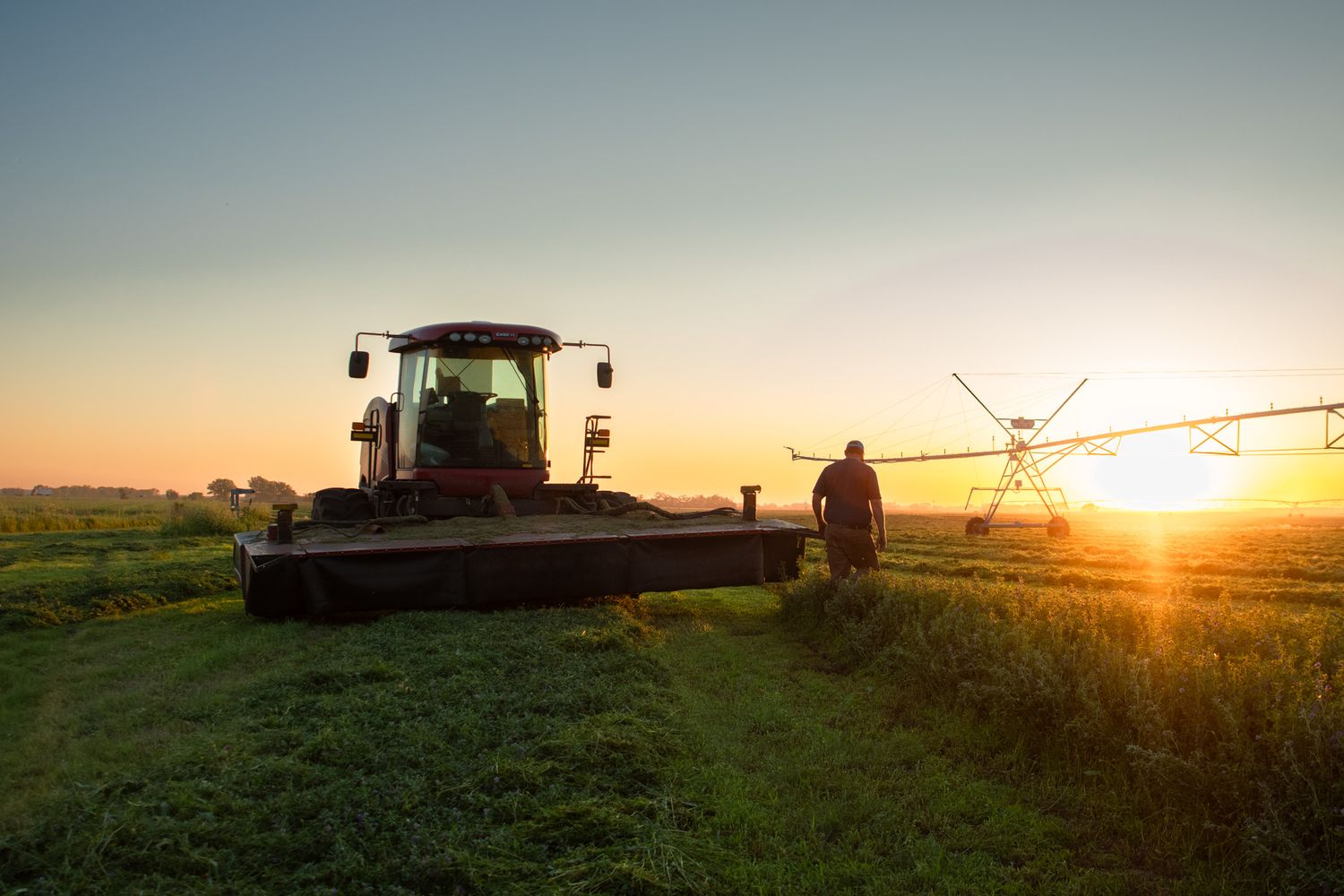 Farmer stands near tractor and irrigation equipment during golden sunset on agricultural field.