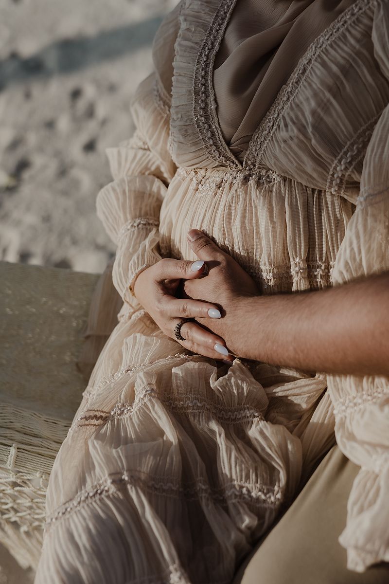 Close-up shot of hands holding delicate vintage lace fabric details in soft beige tones during a luxury pregnancy session.