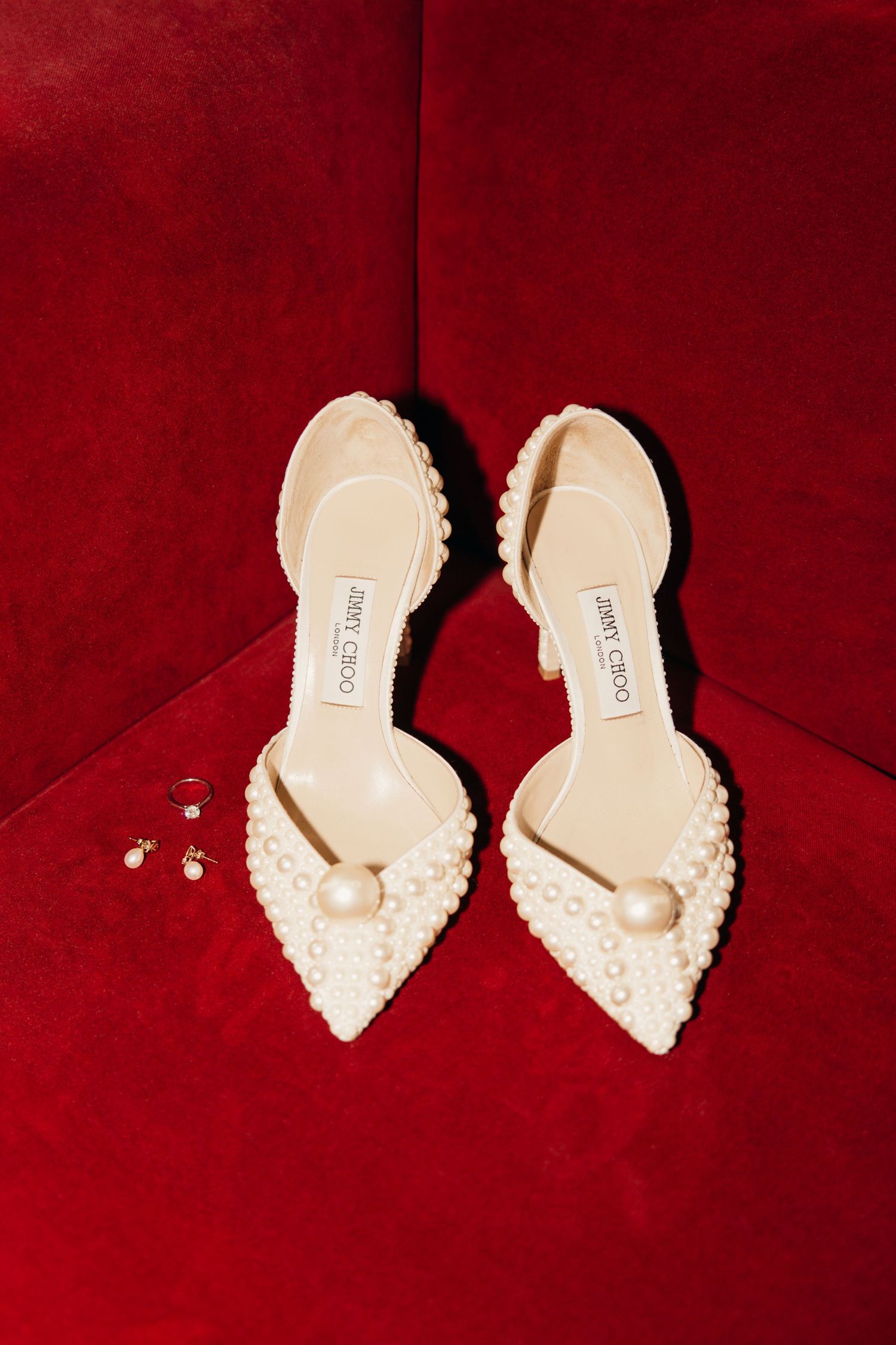 Elegant ivory pearl-embellished bridal shoes displayed on red velvet background.