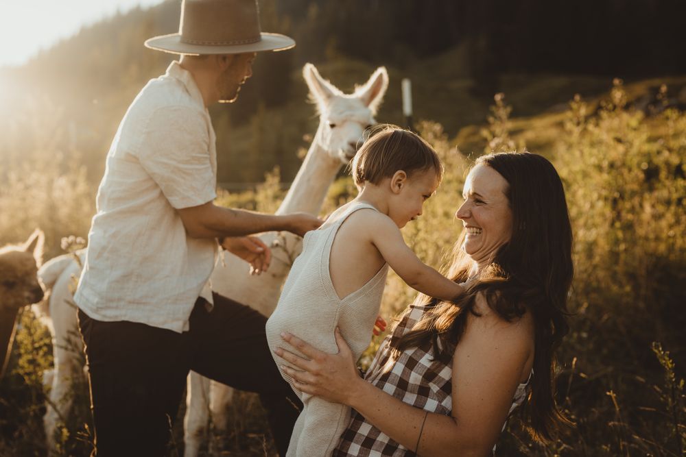 Family stands together in a sun-drenched field during golden hour as sunlight creates a warm, ethereal glow around them.