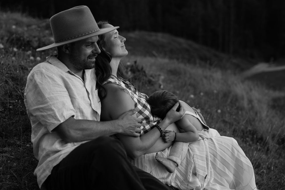 A couple shares an intimate black and white moment together while resting on a grassy hillside.