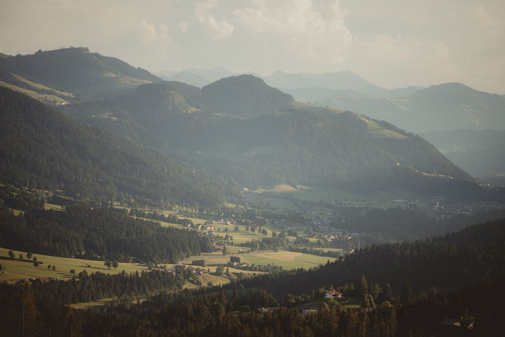 Panoramic mountain landscape with rolling green hills and distant peaks shrouded in morning mist across a valley.