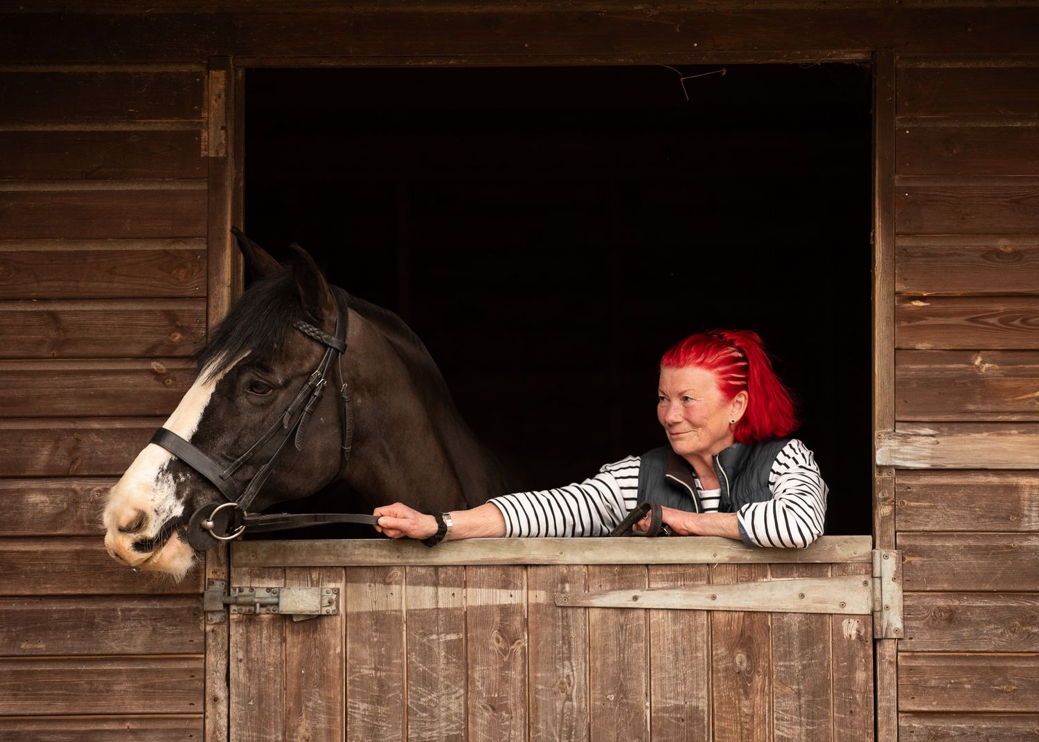 Two riders stand with their animals - a dog and a dark horse relaxing outdoors in a black and white photo.