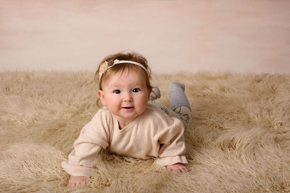 Baby in cream sweater lying on fluffy beige fur during professional photo session.