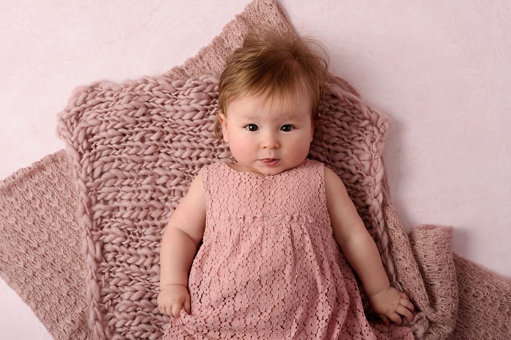 Baby wearing pink knitted lying on matching knit blanket.