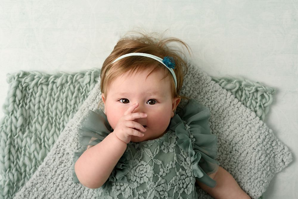 Baby in sage green ruffled outfit lying on knitted blanket during portrait session.
