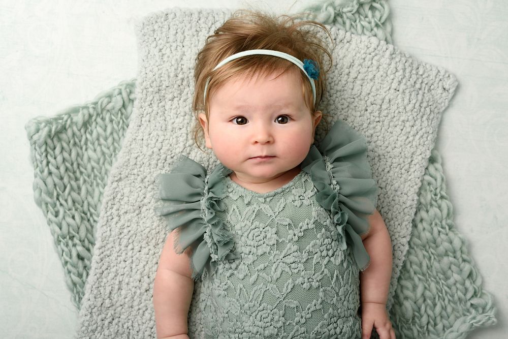Baby wearing sage ruffled romper poses on matching knit blanket.