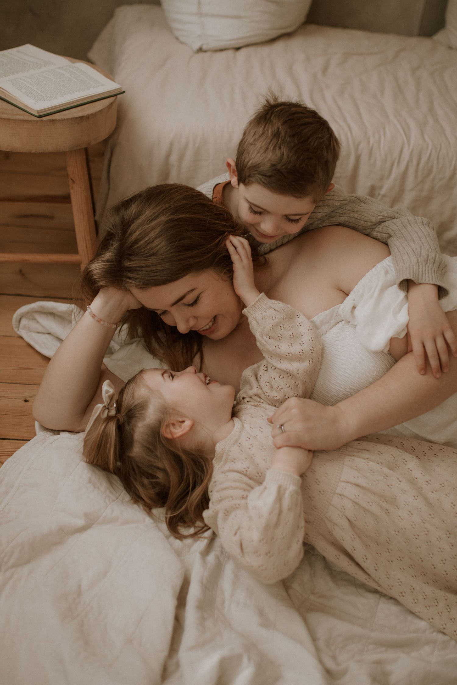 A tender family moment captured in warm sepia tones as they cuddle together on a cozy bed.