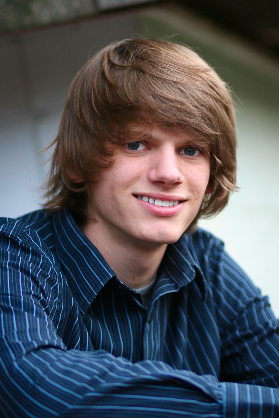 Portrait of someone smiling warmly at the camera while wearing a blue striped button-down shirt.