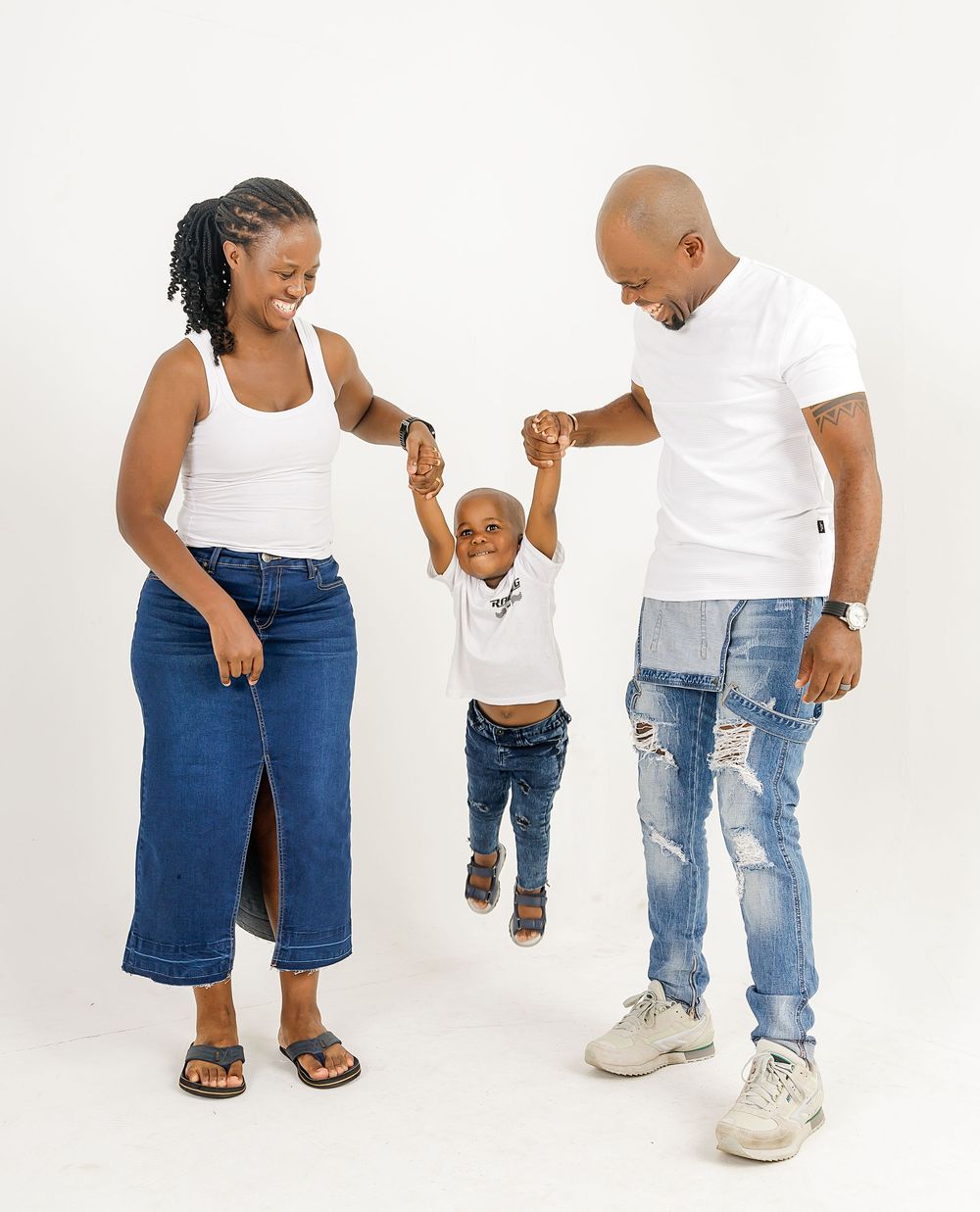Parents and toddler wearing matching ripped jeans and white tops create playful poses in a lifestyle fashion photoshoot.