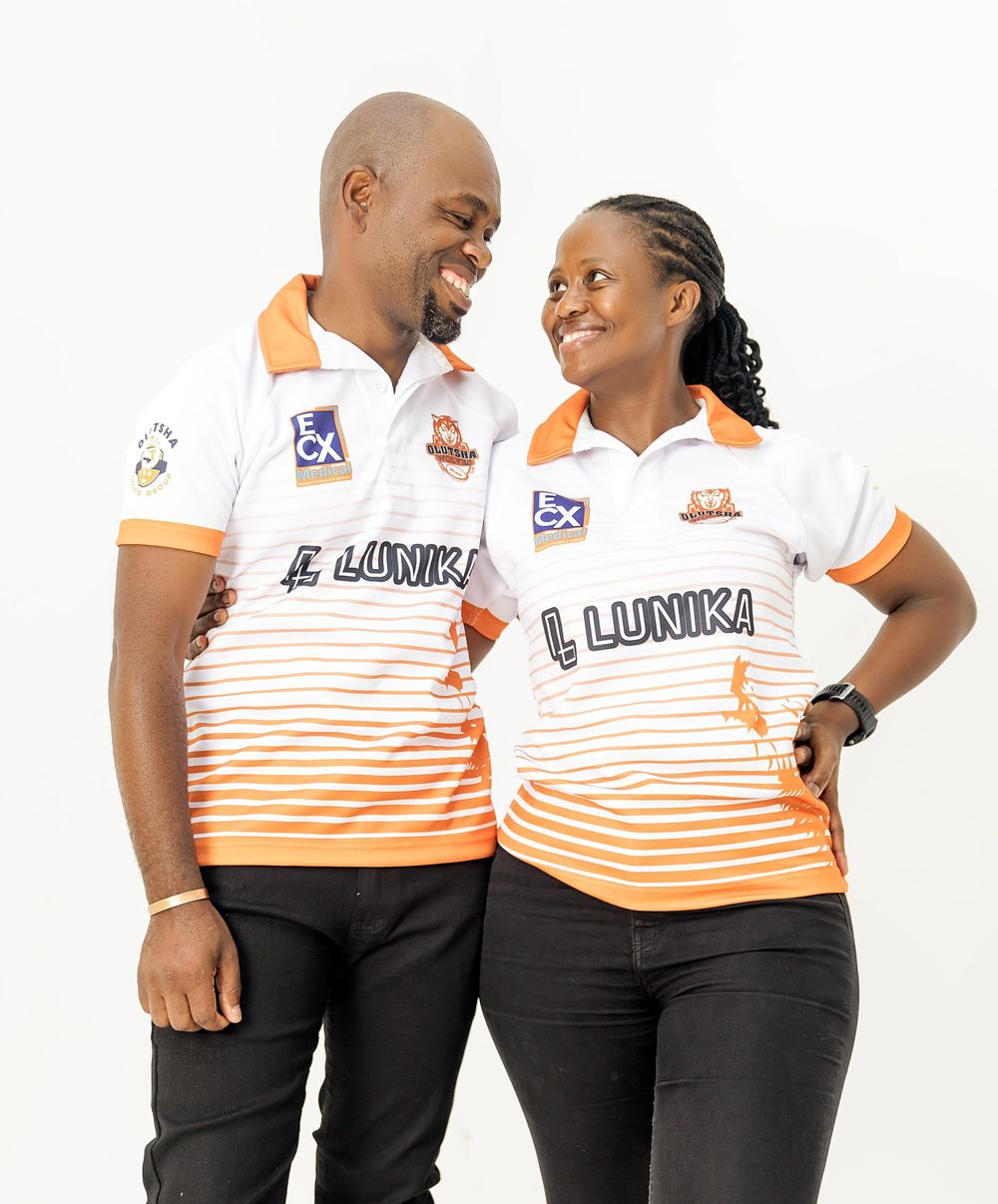 A couple wearing matching white and orange striped polo shirts with Llunika branding smiles warmly at each other.