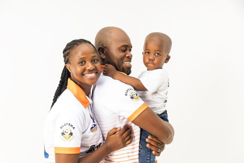 A family in coordinated white and orange polo shirts poses together against a white background.
