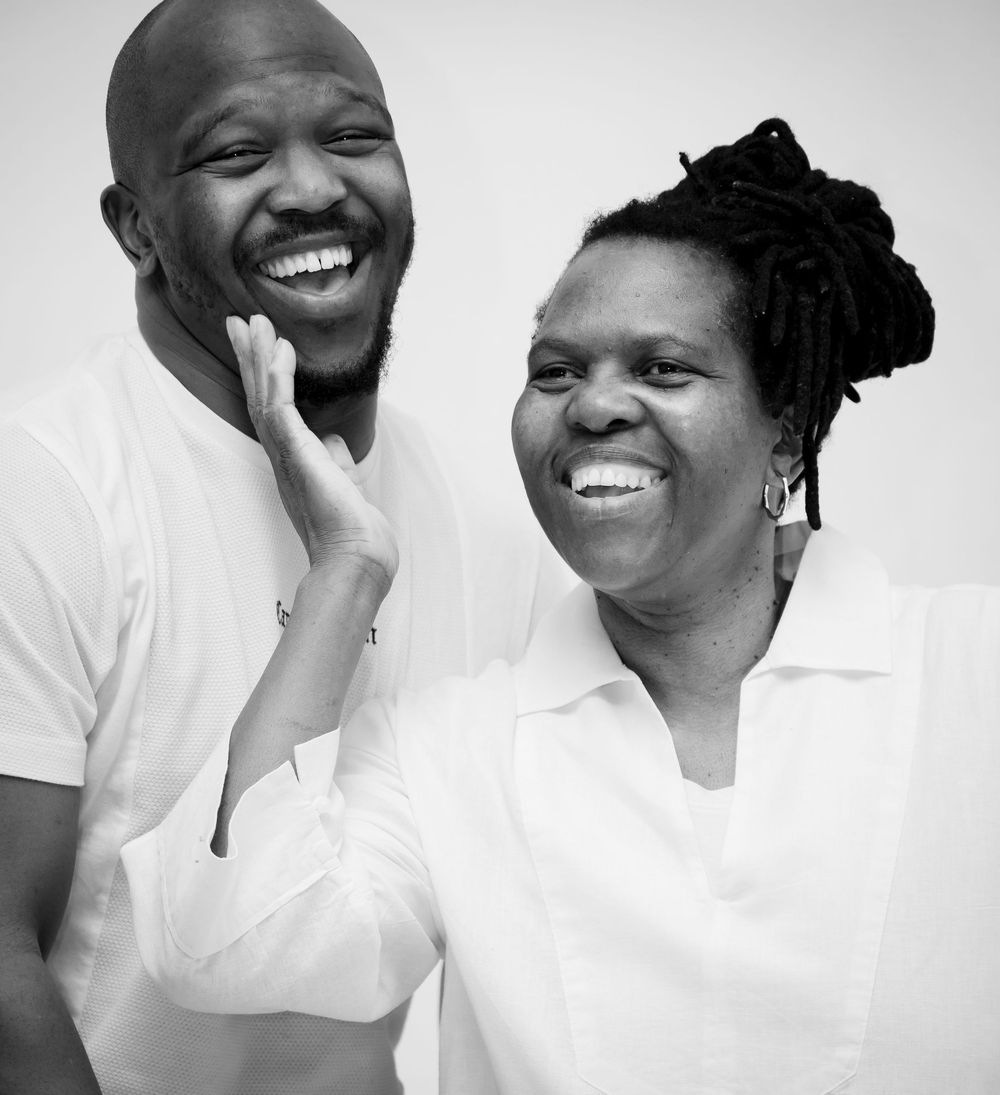 A black and white portrait of two people in white shirts sharing a joyful moment together against a light background.