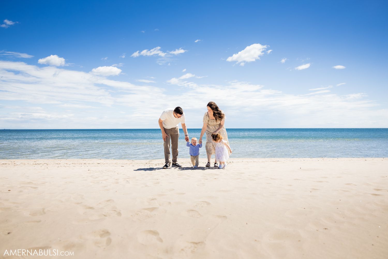 A family stands together on a pristine beach with crystal blue waters and white sand stretching to the horizon.