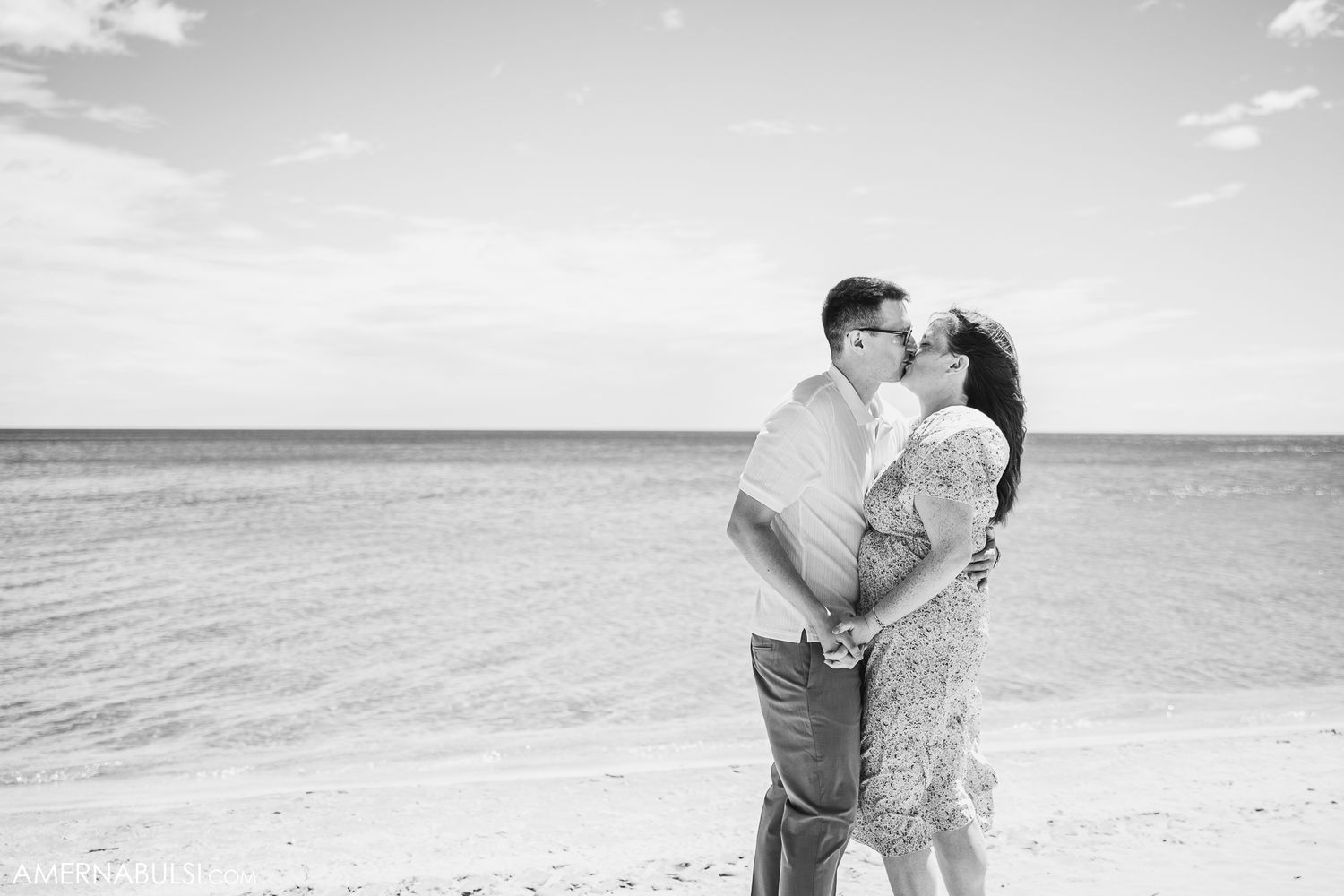 A romantic black and white photograph of a couple embracing on a beach with the ocean in the background.