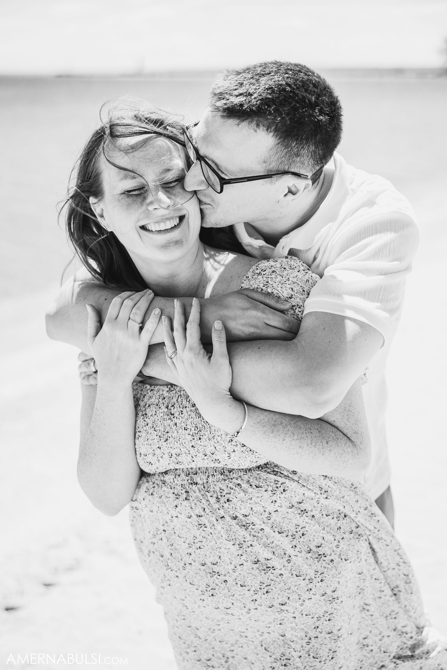 A joyful black and white photo of a romantic embrace with a couple laughing together outdoors.