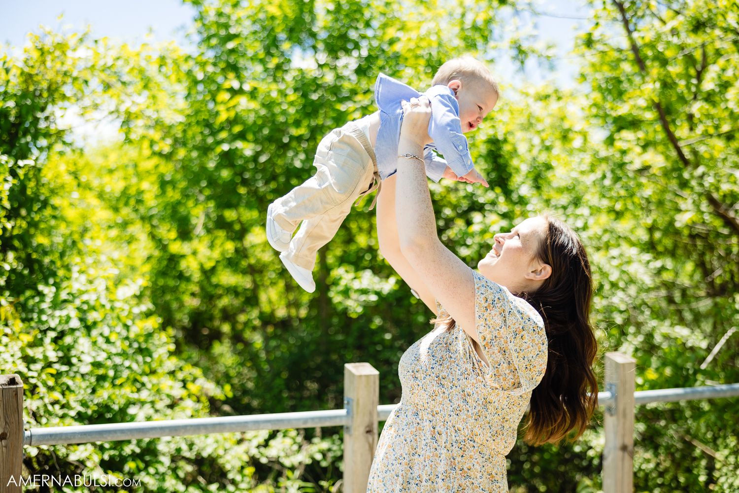 Family enjoying playful moment together in bright sunlit garden during outdoor photo session.
