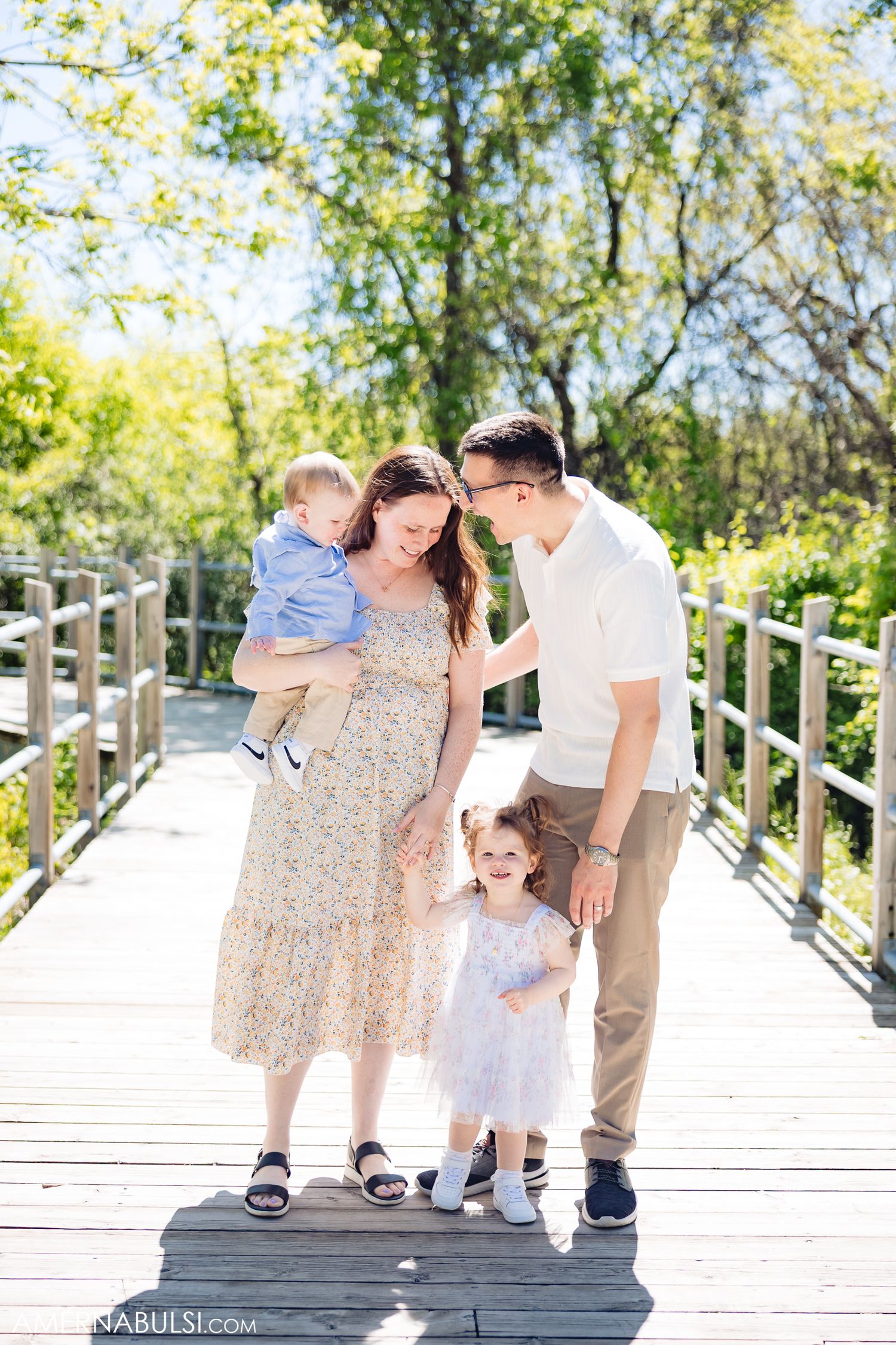 A family enjoying a sunny day together on a wooden boardwalk surrounded by lush green trees.