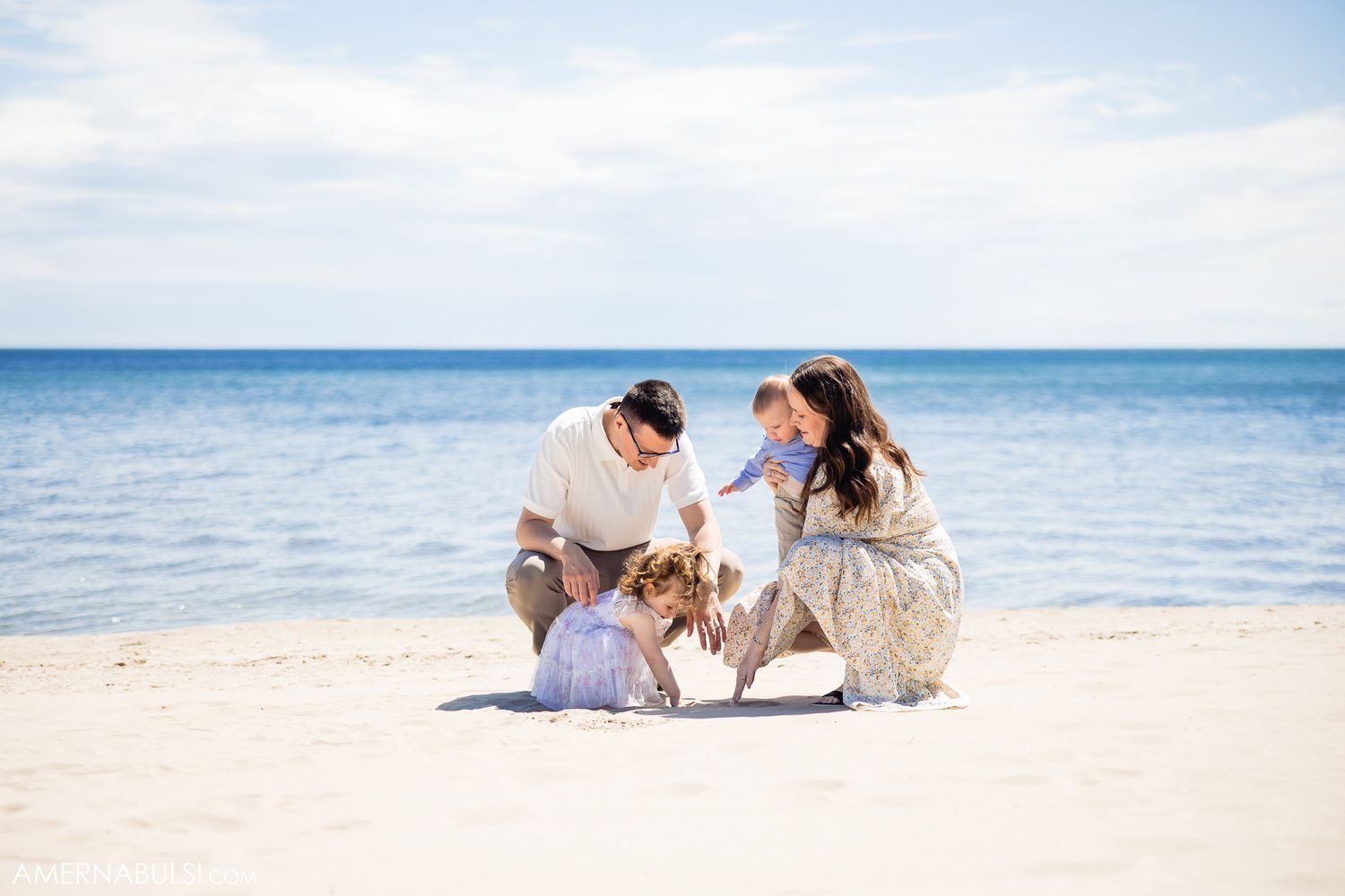 Family relaxing together on white sandy beach with crystal blue ocean waters in background.