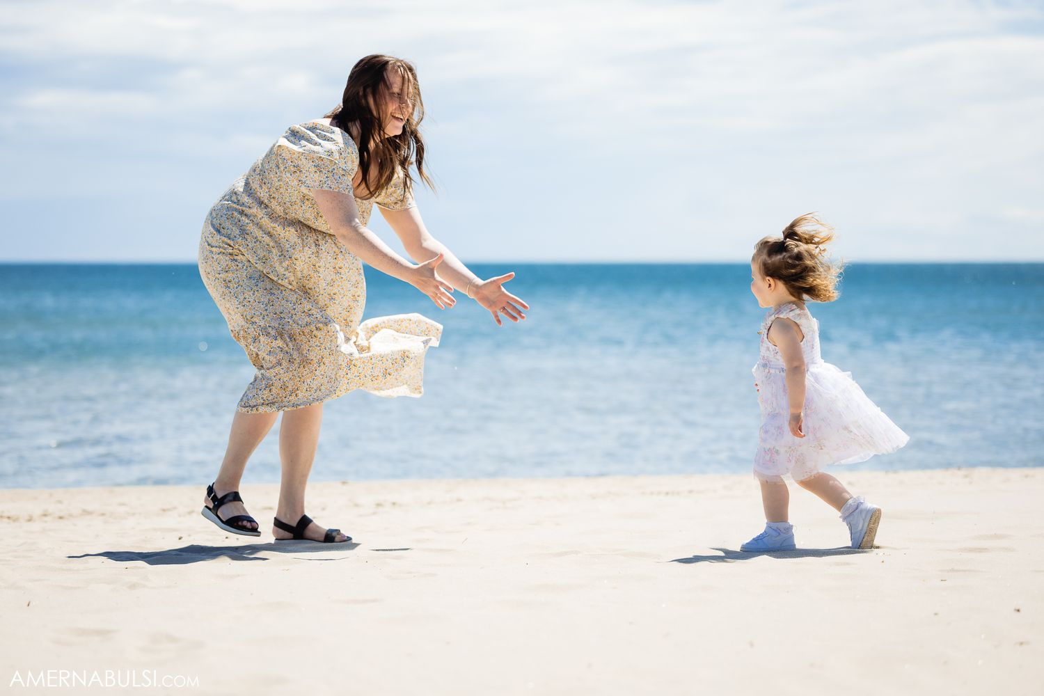 A family plays together on a white sandy beach near clear blue ocean waters.