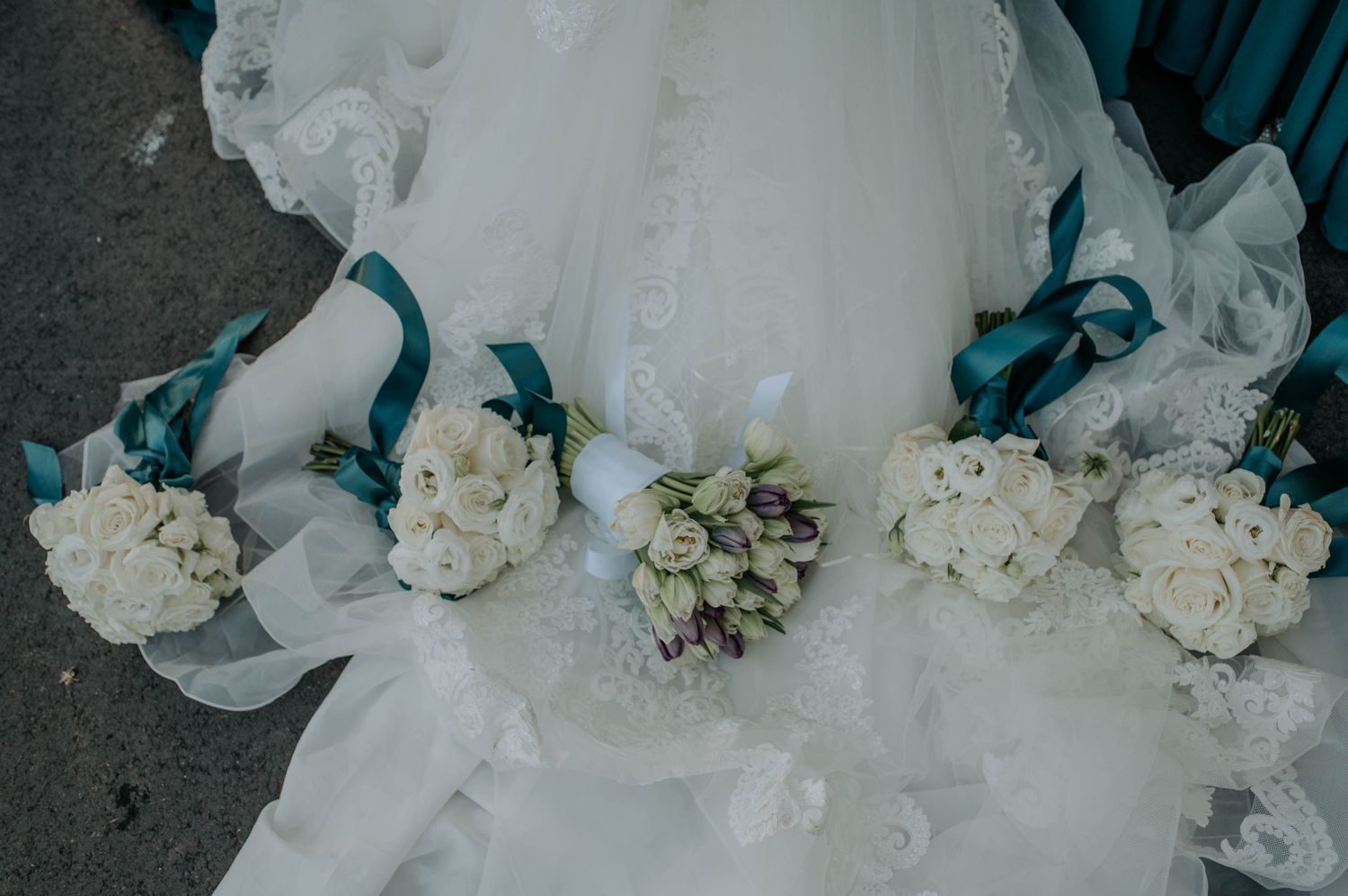 A delicate white tulle wedding dress train adorned with white floral bouquets against a dark rustic surface.