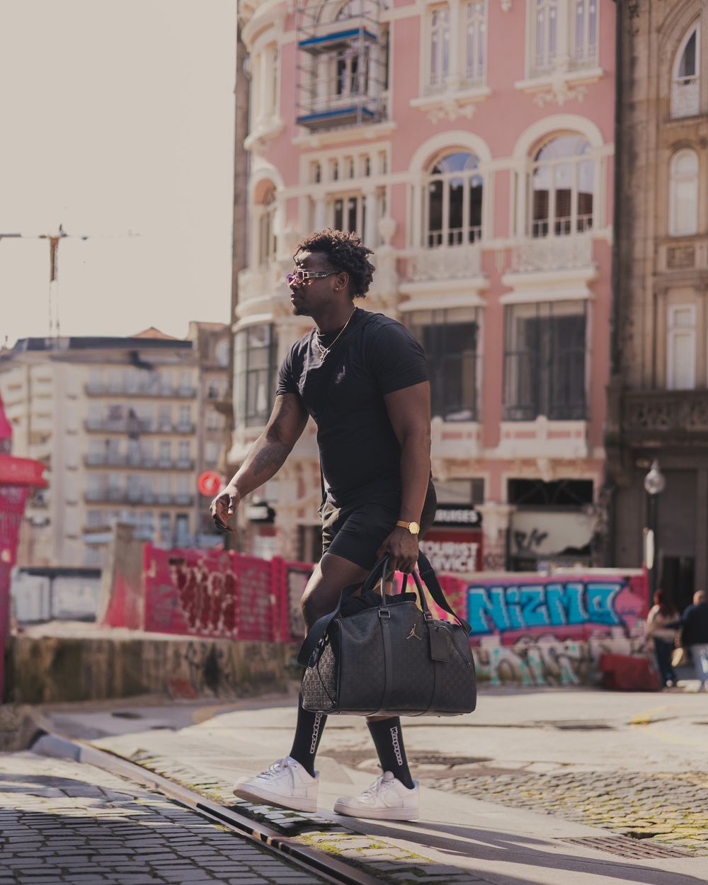 Person walking on street carrying bag near pink building with urban graffiti in background.