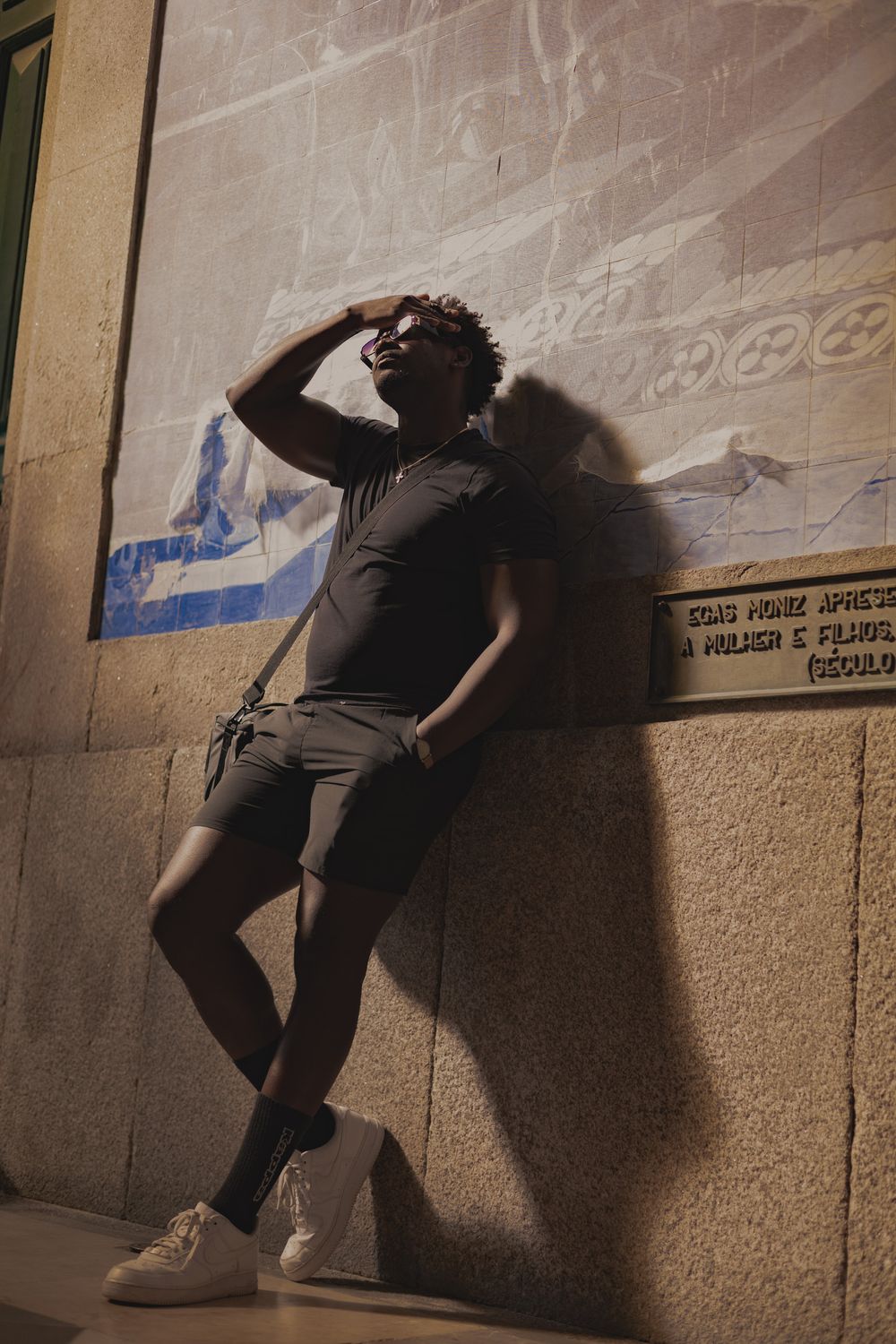Person posing against wall in all black outfit with dramatic shadow effect.