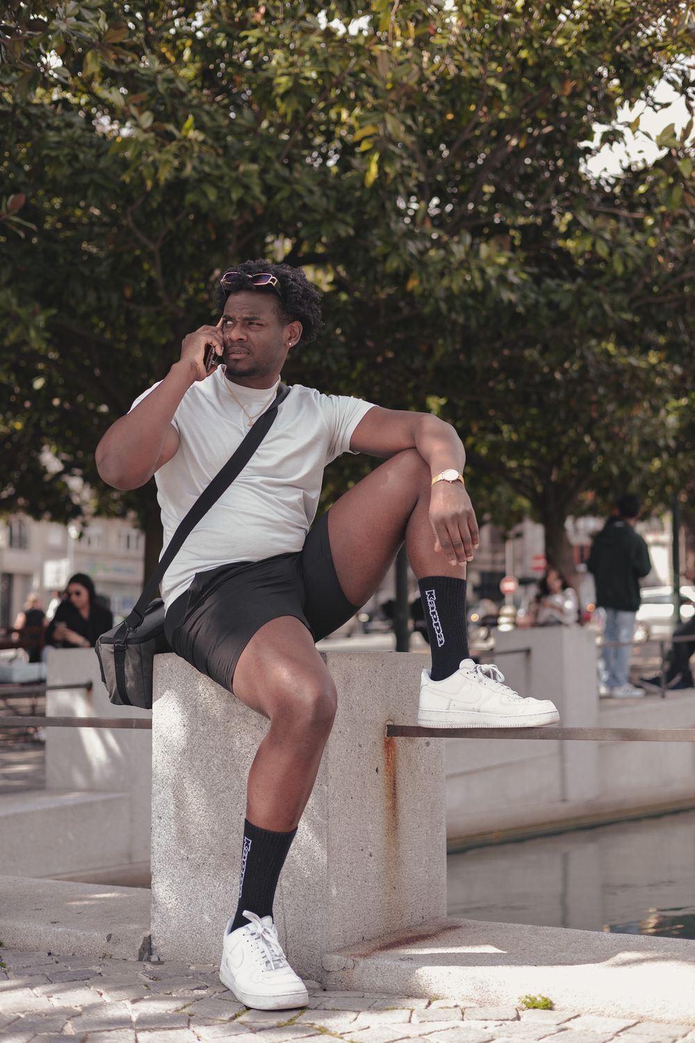 Person sitting on stone ledge in casual summer outfit with white sneakers in urban setting.