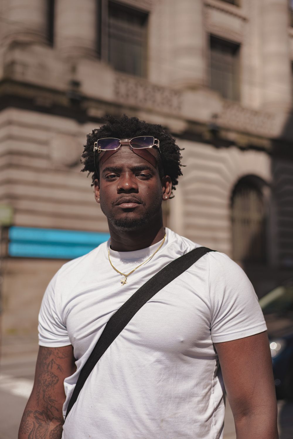 Portrait shot in urban setting with white t-shirt and cross-body bag against architectural backdrop.