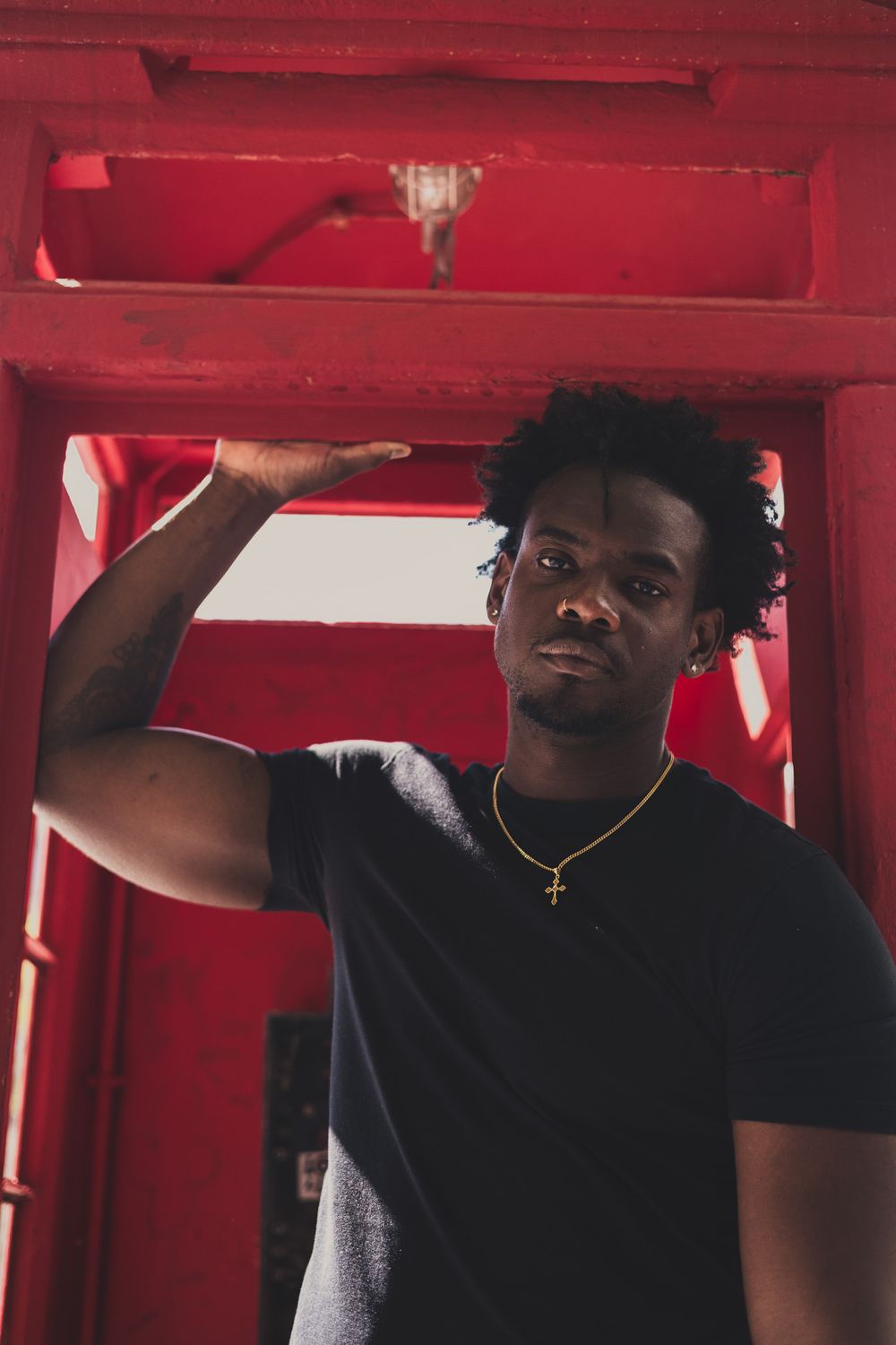 Creative portrait inside red phone booth frame wearing black t-shirt and gold necklace.