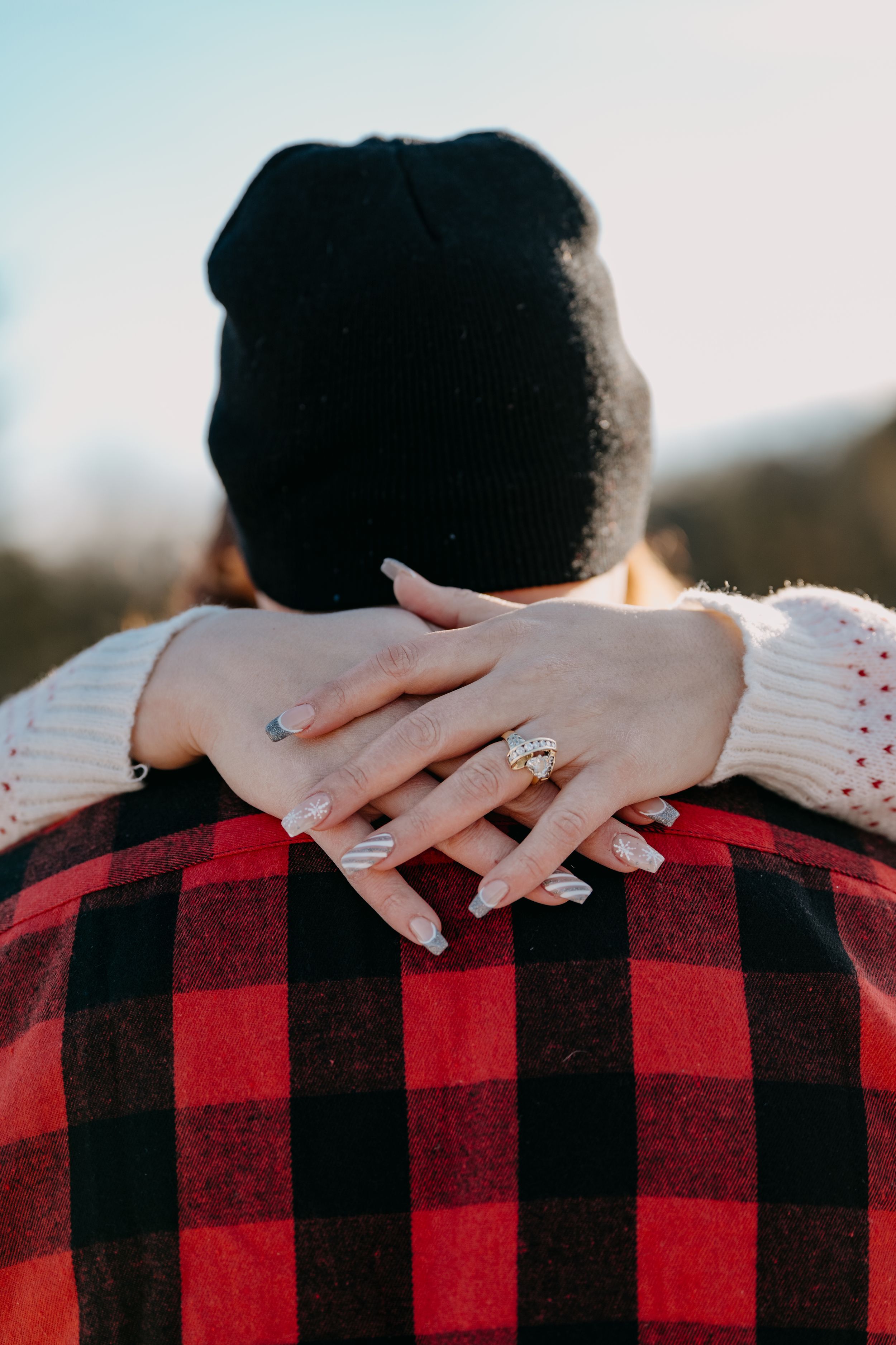 Hands wearing a white sweater embrace someone in a red and black buffalo plaid flannel from behind.