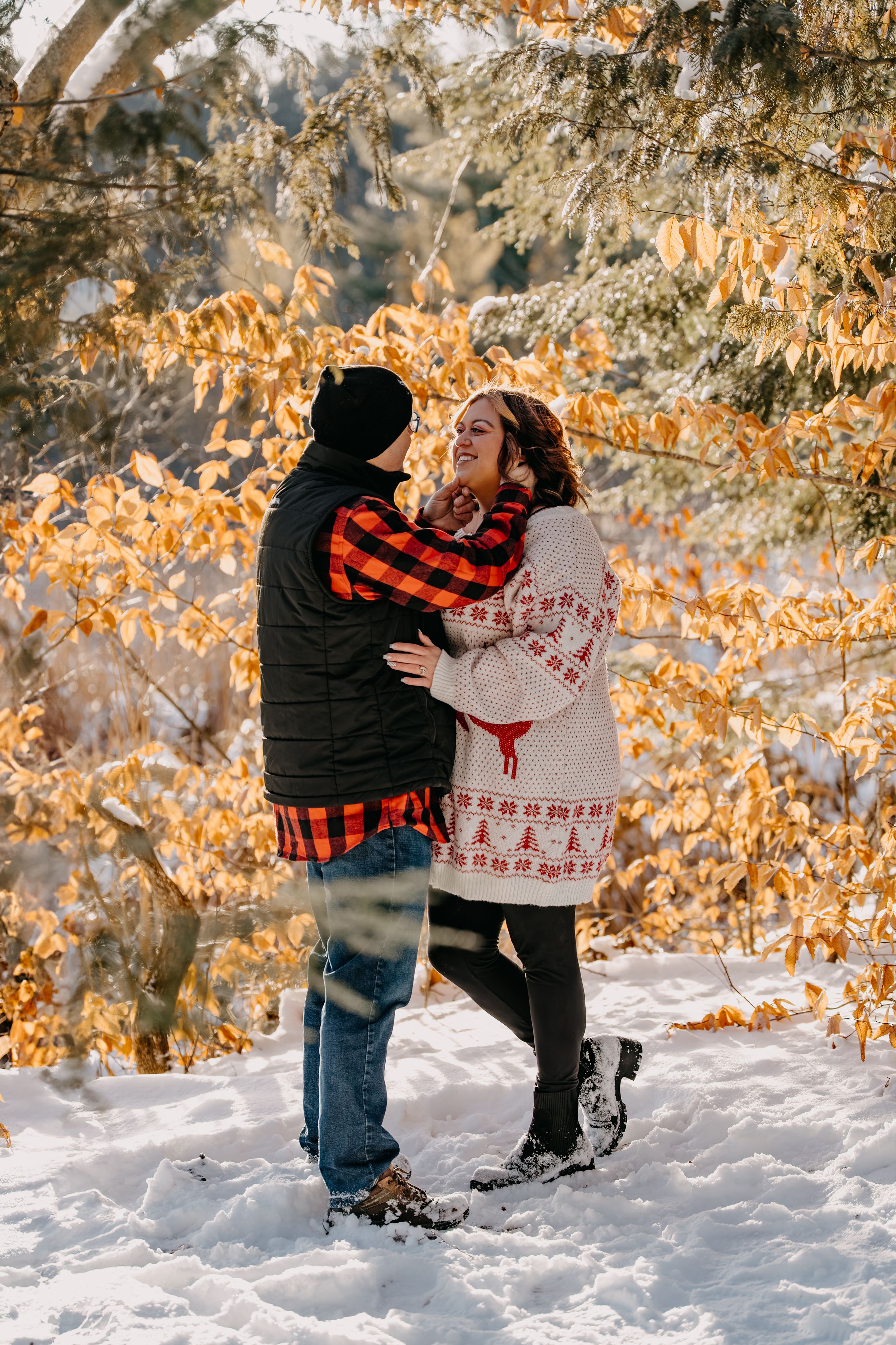 A couple shares a romantic moment in the snow surrounded by golden autumn leaves on a winter day.