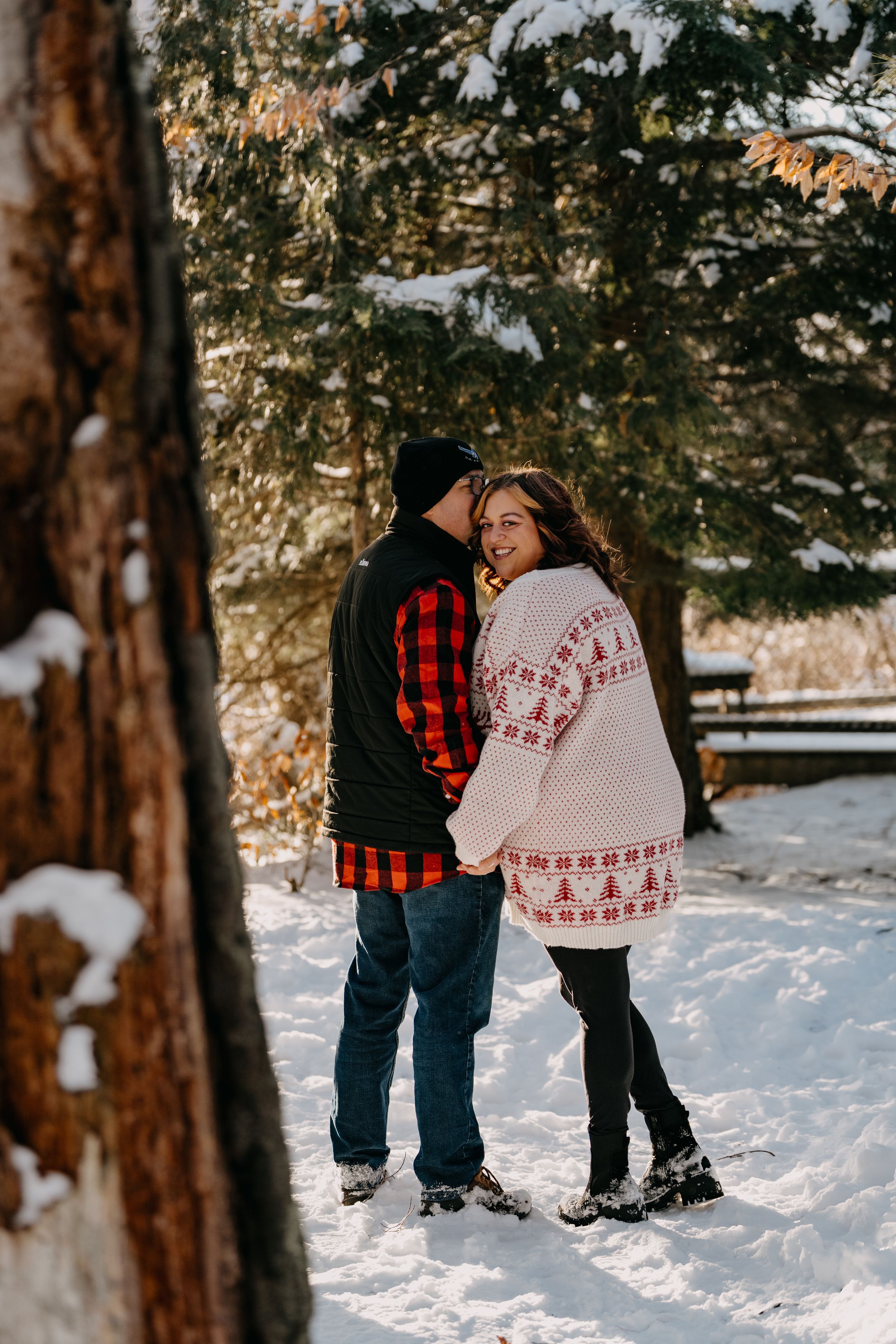 Two people in winter clothes sharing an intimate moment while standing in snowy woods at sunset.