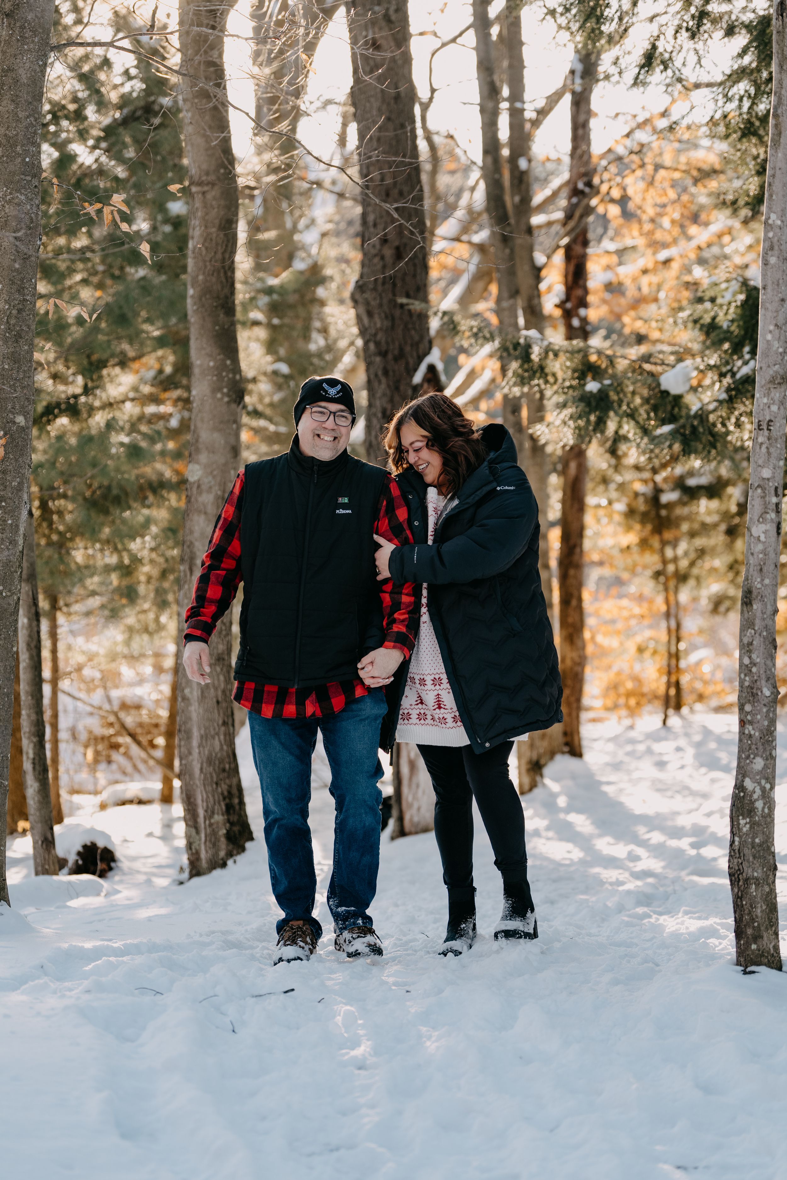 A couple taking a romantic winter walk through a snowy forest path in warm clothing and winter gear.