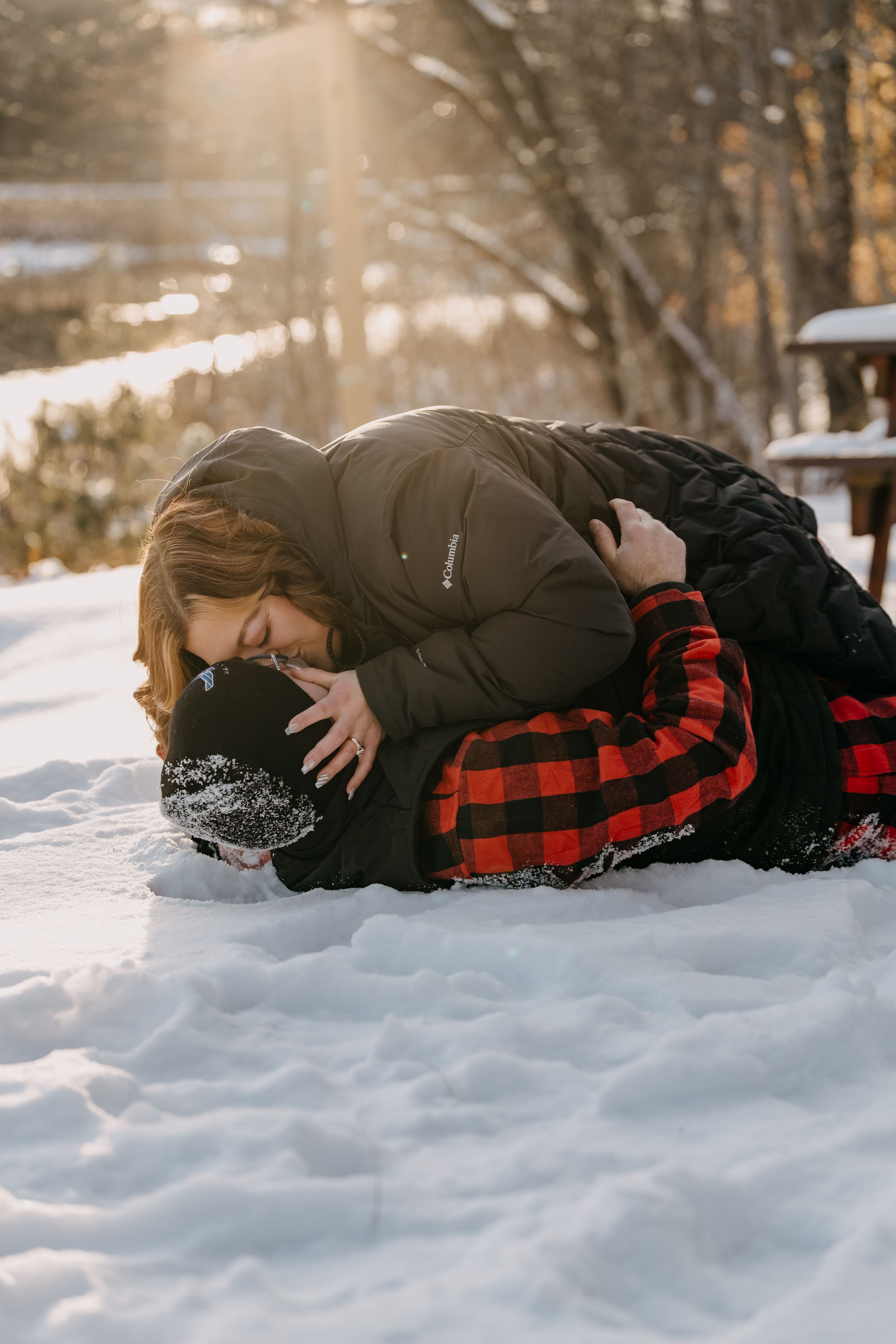 Person in black winter coat and red buffalo plaid pants laying in fresh snow on a bright winter day.