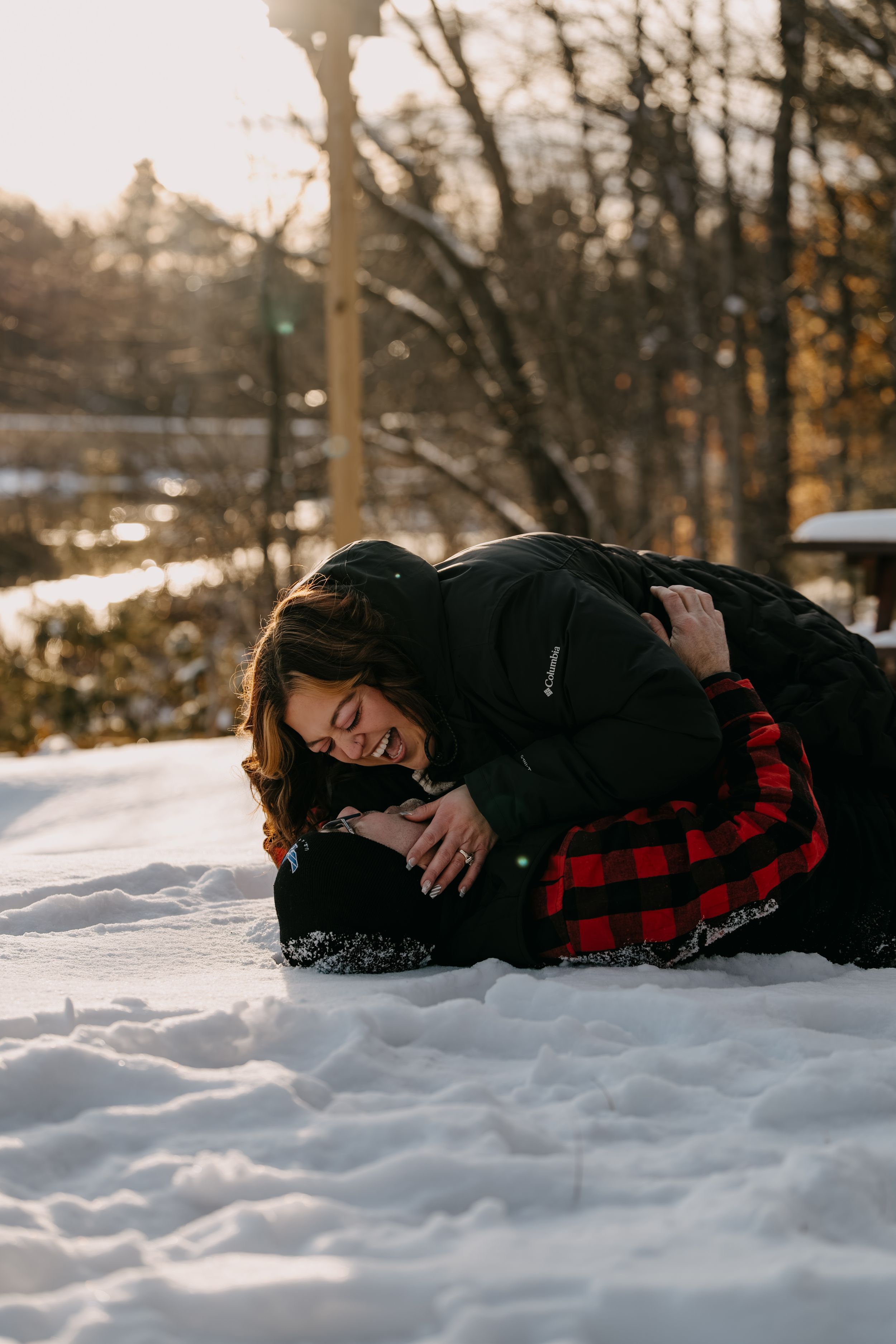 Person in black coat and red plaid pajamas lying in fresh snow during golden winter sunset.