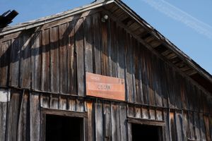 Rustic wooden barn exterior with weathered vertical planks and a slanted roof against a bright blue sky.