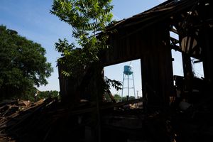 Silhouette of a dilapidated wooden structure with a water tower visible through the ruins against a bright sky background.