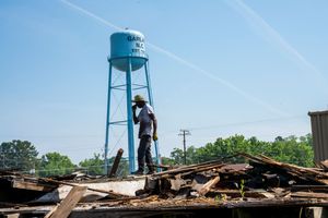 Emergency response personnel surveys storm damage debris with blue water tower in background under clear sky.