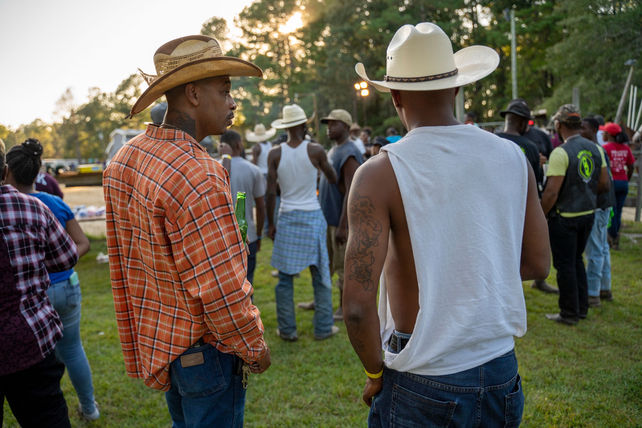 People in cowboy hats and western attire gather outdoors at a community event during sunset.