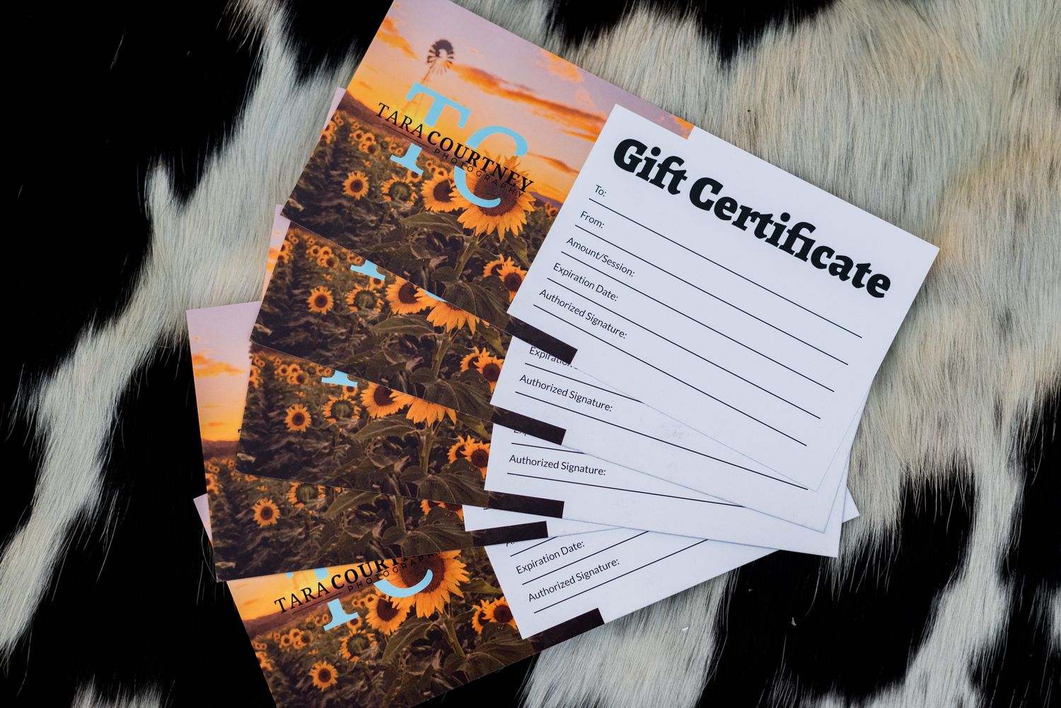 Multiple gift certificates displayed over a black and white cowhide leather surface during sunset.